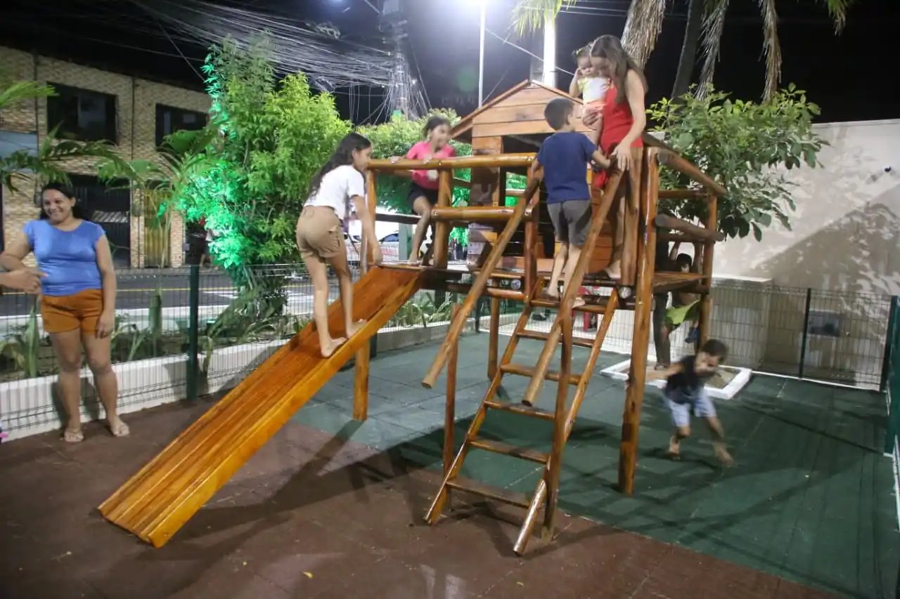 A foto mostra parte do parquinho da praça sendo utilizado por crianças