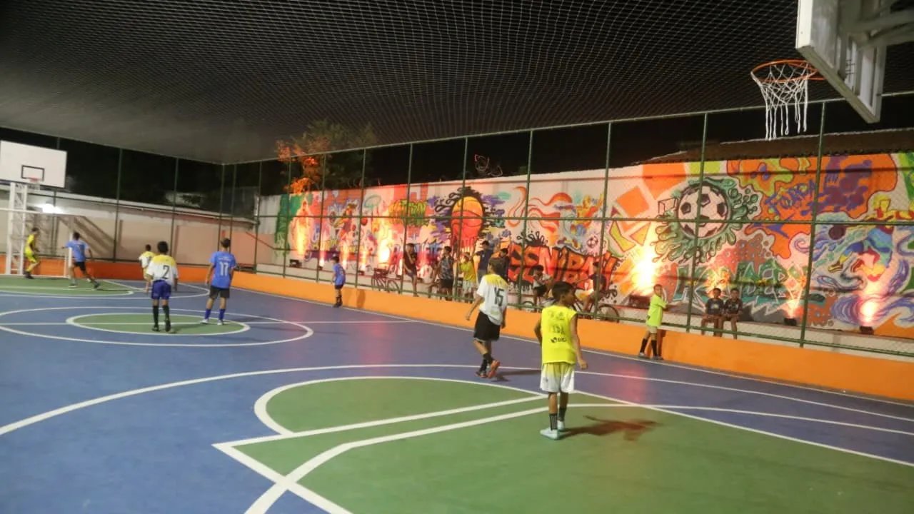 A foto mostra a quadra poliesportiva da Praça requalificada. Nela, alguns rapazes jogam futebol